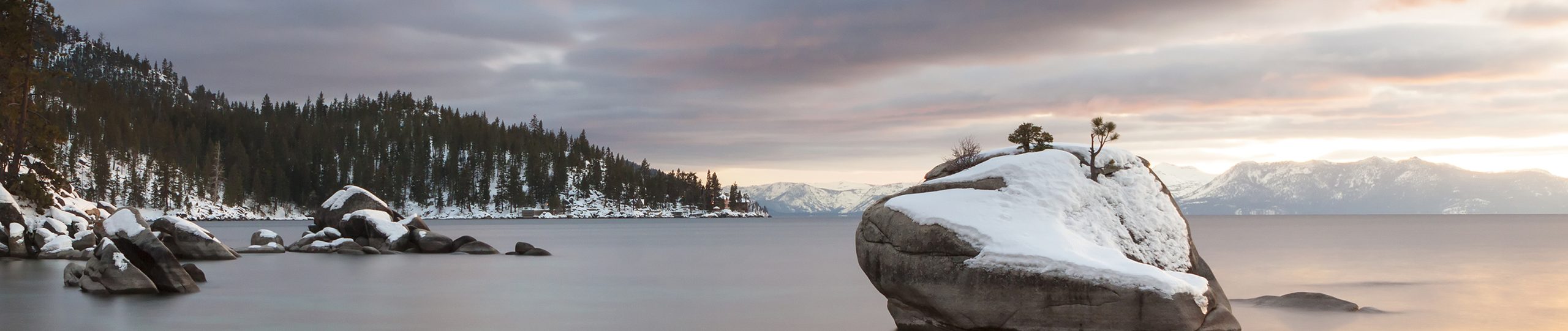 Pleasant Lake Tahoe weather with snowy boulders on lake at sunset